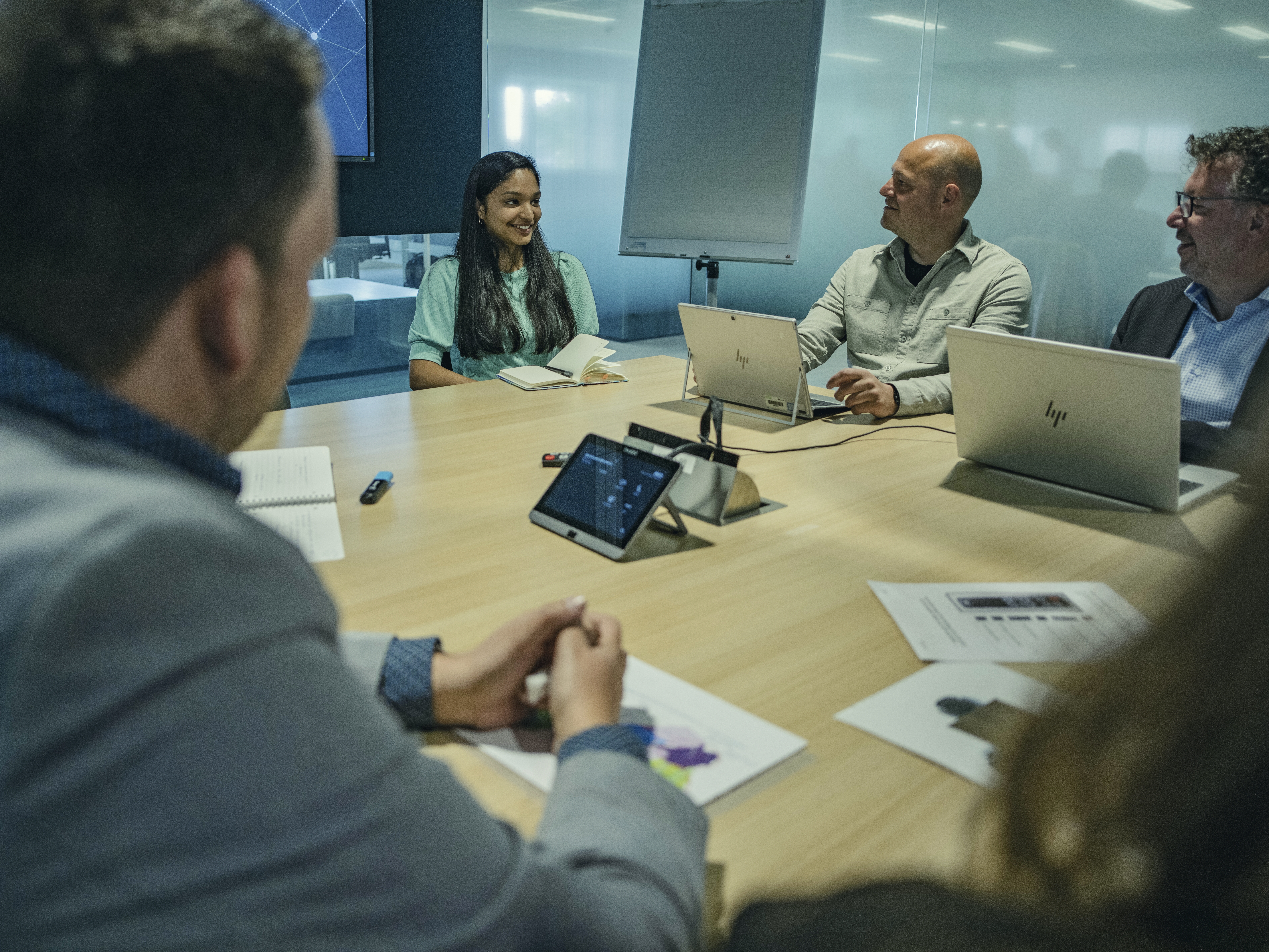 Laptops op de tafel van de vergaderruimte waarin de monitor wordt besproken met verschillende personen.